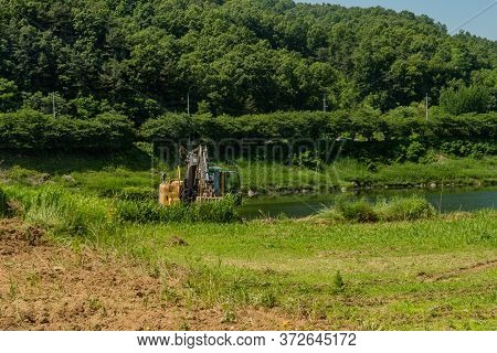 Cheongju, South Korea; May 31, 2020: Single Backhoe Sitting Idle In Tall Grass In Countryside Beside