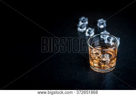 Whisky, Whiskey, Bourbon Or Cognac With Ice Cudes On Black Stone Table
