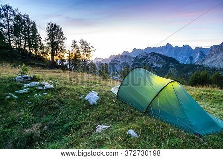 A Tent Glows Under A Moon Night Sky At Twilight Hour. Julian Alps, Triglav National Park, Slovenia.