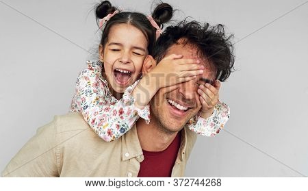 Indoor Image Of Playful Daughter Covers The Eyes With Hands Of Her Father For A Surprise On Father's