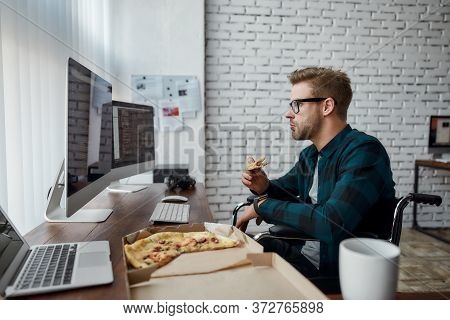 Caucasian Male Web Developer In A Wheelchair Eating Pizza And Looking At Multiple Computer Screens W