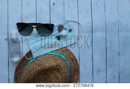 Straw Hat, Sunglasses, Pebbles, Medical Mask And Antiseptic On A Wooden Background. The Tourist Cris
