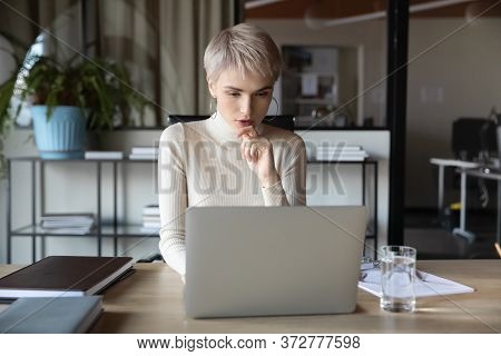 Concentrated Businesswoman Working Using Laptop Sitting At Desk In Office