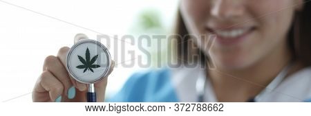 Close-up Of Female Hand Holding Stethoscope With Cannabis Sign. Smiling Doctor Practitioner In Medic