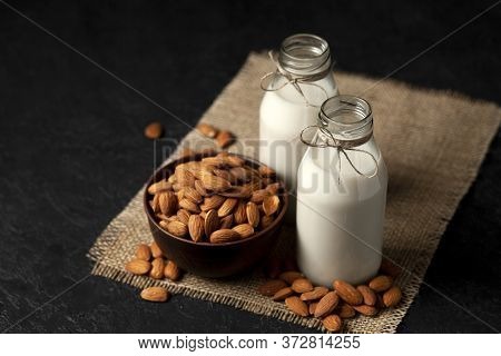 Two Bottles Of Almond Milk With Nuts On A Dark Black Table, Vegetarian Milk Without Sugar And Lactos
