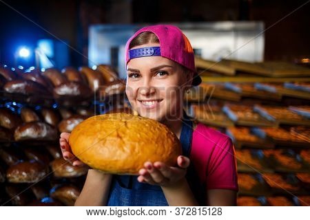 The Stage Of Baking In A Bakery. Portrait Of A Baker Girl With Bread In Her Hands Against The Backgr