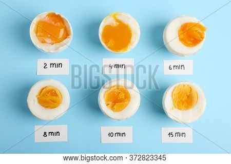 Different Cooking Time And Readiness Stages Of Boiled Chicken Eggs On Light Blue Background, Flat La