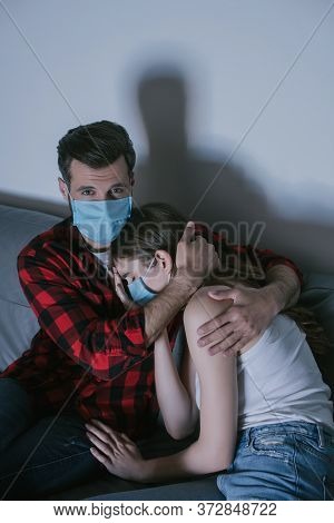 Couple In Medical Masks Watching Tv While Man Hugging Upset Girl