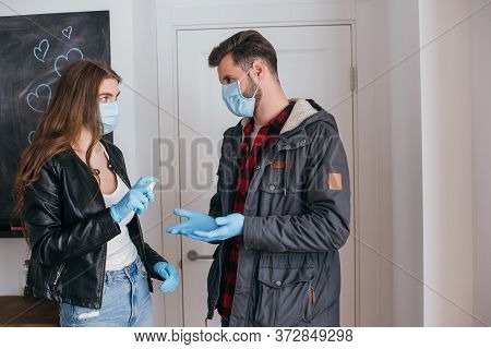 Couple In Medical Masks And Latex Gloves Using Antiseptic Spray