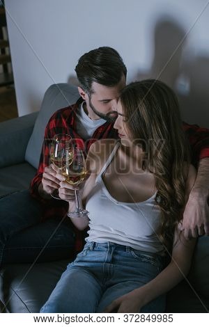 Angle View Of Happy Young Couple Sitting On Couch With Glasses Of White Wine