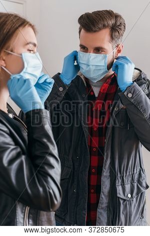 Couple In Latex Gloves Putting On Protective Masks Before Leaving Home