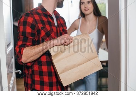 View Of Young Man Holding Paper Bag With Takeaway Food While Looking At Pretty Girlfriend
