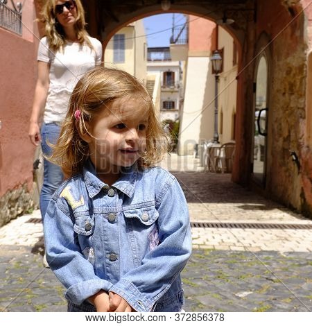 Portrait Of Pretty Little Girl In The Italian Village. Her Mum On The Background. San Felice Circeo,