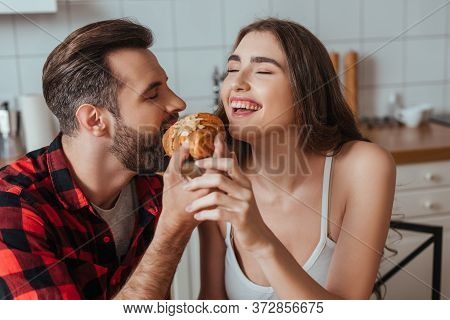 Young Woman Laughing With Closed Eyes While Boyfriend Eating Delicious Croissant
