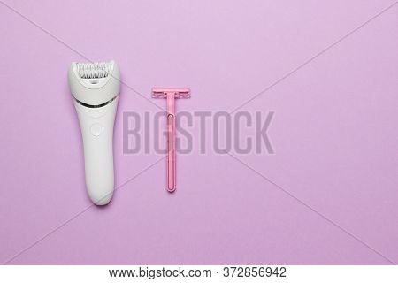 Women Epilator And Pink Razor On Purple Colored Paper Background, Top View With Copy Space.