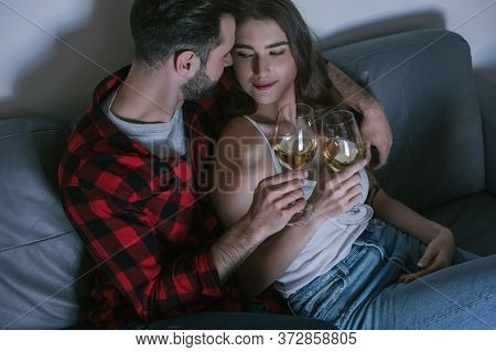 Angle View Of Happy Couple Clinking Glasses Of White Wine While Sitting On Sofa