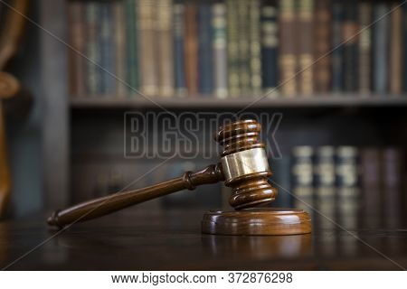 Judge Office. Gavel On Brown Shining Table And Collection Of Legal Books In The Bookshelf.