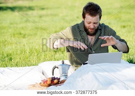 Man Sneezing While Working On His Laptop, Sitting In Bed Outdoors In Grassfield