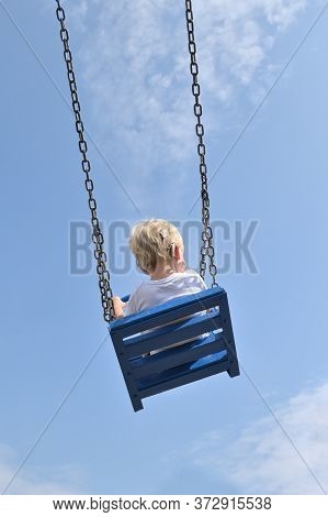 A Boy With Cochlear Implants Riding Swing In Summer Park