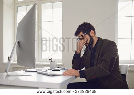 Exhausted Tired Worker At The Workplace Covered His Face With His Hands In The Office