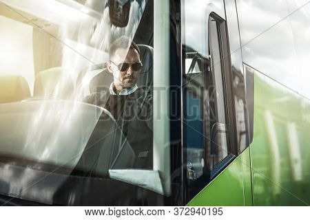Caucasian Bus Driver Behind The Wheel Of Modern Vehicle. Coach Bus Driving Theme. Public Transportat