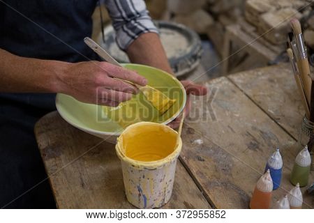 Mid-secion of male potters hand painting a bowl in pottery workshop
