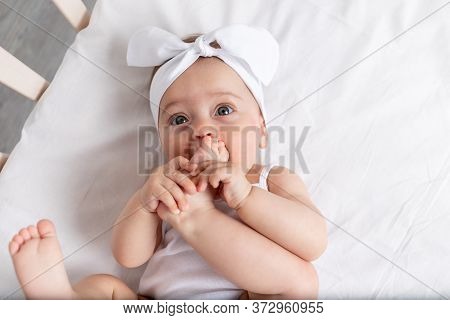 Baby Girl 6 Months Old Lies In A Crib In The Nursery With White Clothes On Her Back And Laughs, Look