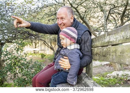 Father And Little Son Sitting On The Wooden Bench