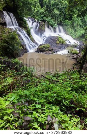 Waterfall Landscape View Of Fresh Water Flows Over A Vertical Drop To Green Field In Tropicana