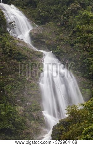 Waterfall Landscape View Of Fresh Water Flows Over A Vertical Drop To Green Field In Tropicana