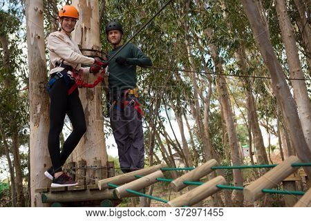 Portrait of smiling couple holding zip line cable standing on wooden platform in the forest