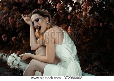 The Bride In A White Dress Is Crying, Holding A Cigarette In Her Hands, Holding A Bottle Of Alcohol.