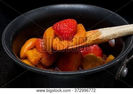 Picking Up Some Apricot And Strawberry Jelly In The Making In A Non-stick Pan On Top Of A Stove