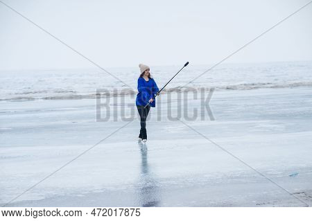 A Caucasian Woman Is Skating On A Frozen Lake Holding A Selfie Stick In Her Hands. The Figure Skater