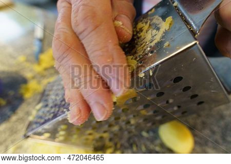 An Older Woman Grating A Potato On A Grater