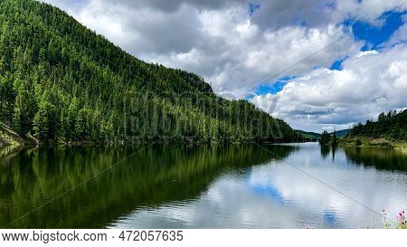 A Mountain Lake With A Black Water Surface And A Green Forest.