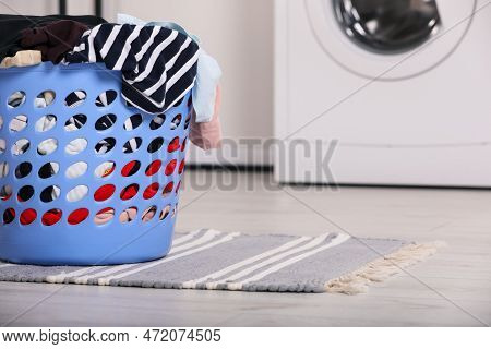 Plastic Laundry Basket Overfilled With Clothes In Bathroom. Space For Text