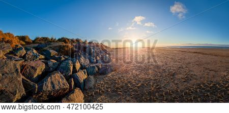 Stunning Sunset At Brancaster Beach With Sand And Sea Defence Rocks. Panoramic Scenic Landscape In N