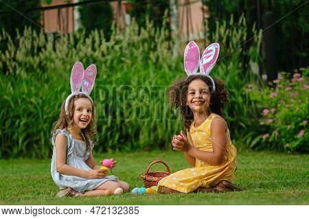 A Two Girls During Easter Egg Hunt And Putting Easter Eggs In Baskets