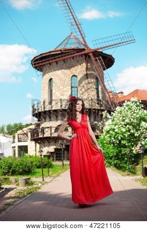 Krásná žena v zářivě červených šatech na pozadí mlýna