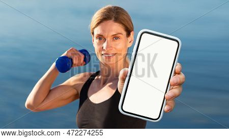 Sporty Middle Aged Woman Training With Dumbbells Outdoors And Showing Blank Smartphone