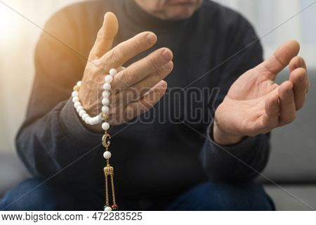 An Elderly Man Prays With A Rosary And The Flag Of The United Arab Emirates