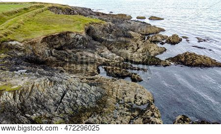 A Picturesque Stone Cape Covered With Green Grass. A Rock On The Seashore. The Rocky Coast Of The At