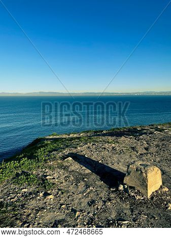 A Stone Geological Marker Casting A Dramatic Afternoon Shadow On A Bluff Overlooking The Pacific Oce