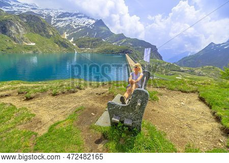 Backpacker Woman Resting On A Bench Of Lakefront Of Lake Robiei And Dam. Swiss Reservoir In Maggia V