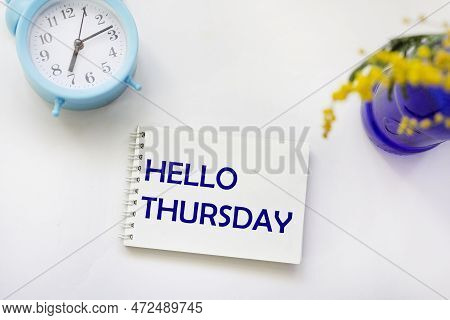 Hello Thursday Words On A Notepad And A Bouquet Of Mimosa Flowers In A Blue Vase On A White Table Wi