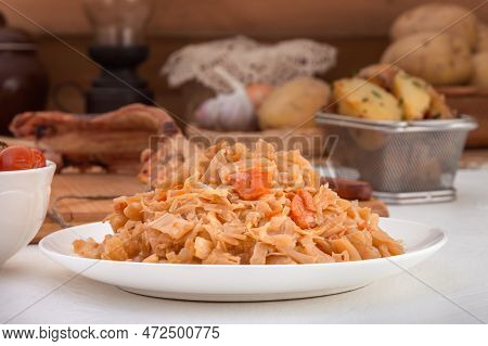 Stewed Cabbage - Bigos In A White Porcelain Plate On The Background Of A Piece Of Smoked Meat And Ba