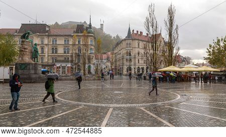Ljubljana, Slovenia - November 4, 2019: People Walking With Umbrellas Over Wet Square In Capital Cit