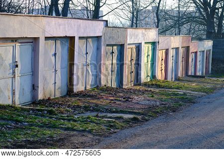 Row Of Concrete Garages With Colorful Metal Doors Along A Road Through Urban Park With Trees. Suburb
