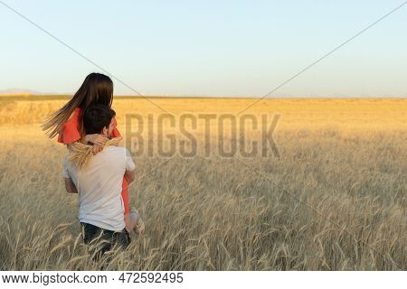 A Young Man Picked Up His Woman In His Arms And Carries Her On Sunset In Wheat Field.